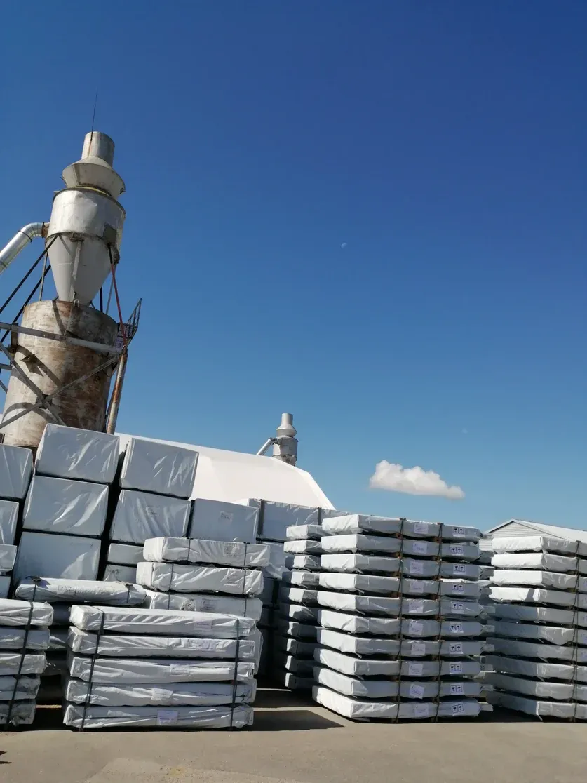 Stacks of wrapped building materials outside under a clear blue sky with industrial equipment in the background.